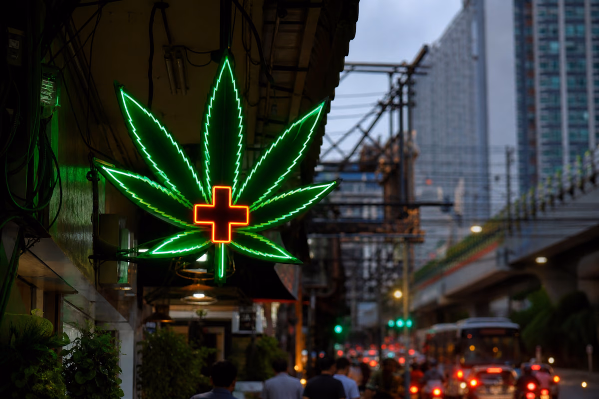 Enseigne néon en forme de feuille de cannabis avec une croix médicale dans une rue animée de Bangkok